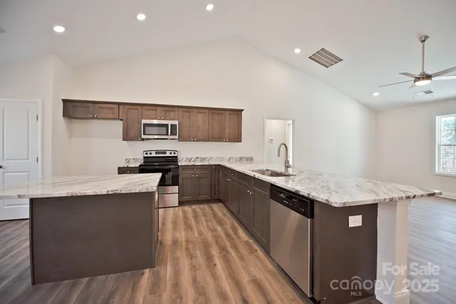 a kitchen with stainless steel appliances granite countertop a sink dishwasher a stove and a refrigerator with wooden floor