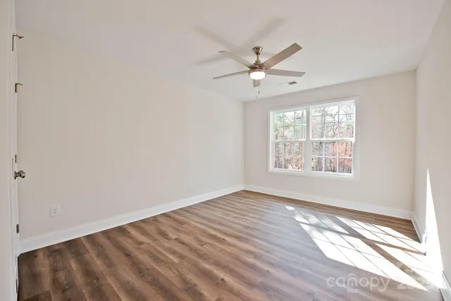an empty room with wooden floor fan and windows