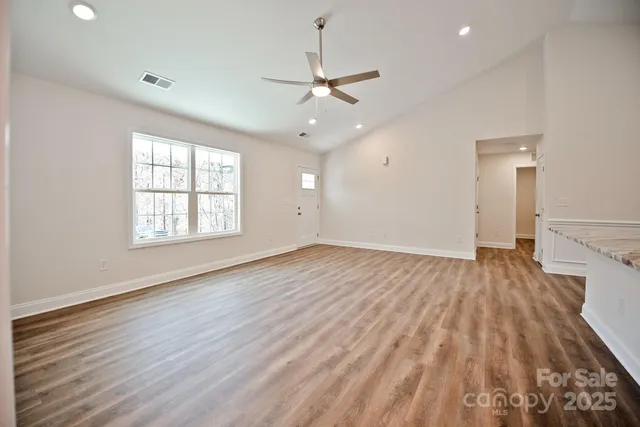 an empty room with wooden floor a ceiling fan white walls and windows