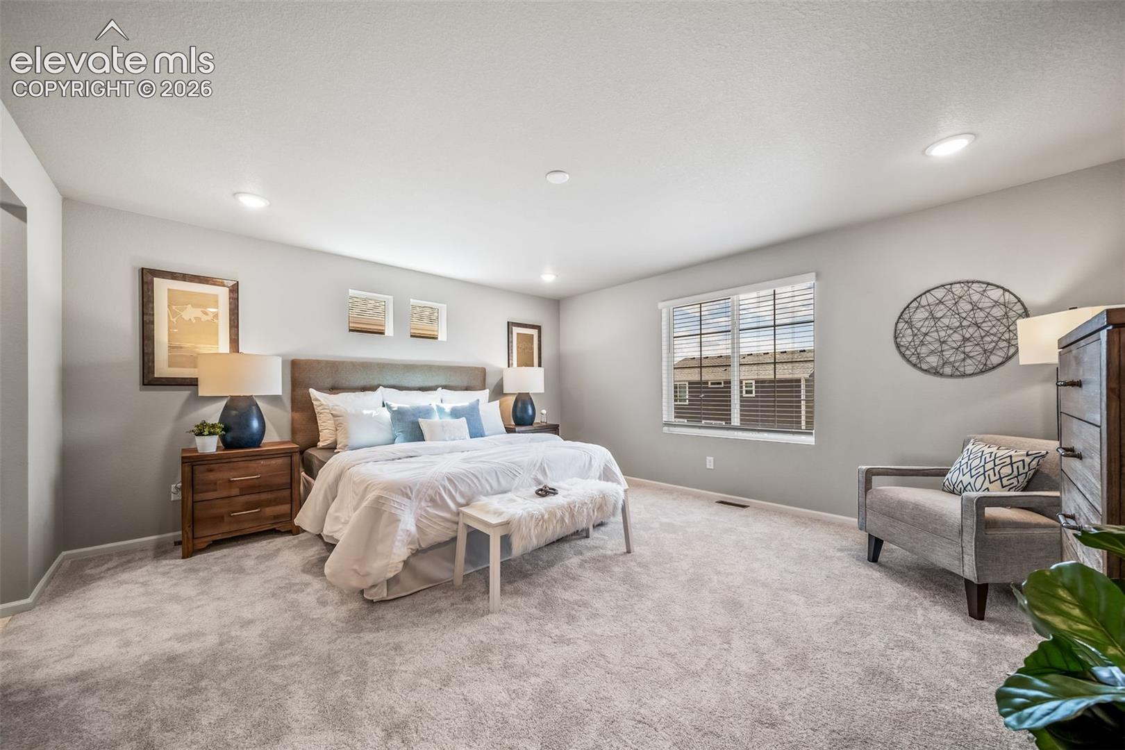 4866 Truscott Road Colorado Springs, CO 80925 - Photo 18 of 20 Spacious bedroom featuring light gray carpeting, recessed lighting, and a large window with blinds
*Photos of a model home*