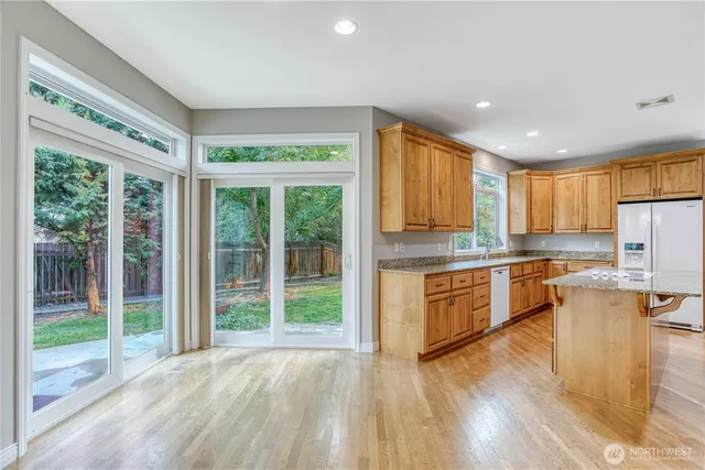 a kitchen with stainless steel appliances granite countertop a refrigerator a sink dishwasher a stove and a large window with wooden floor