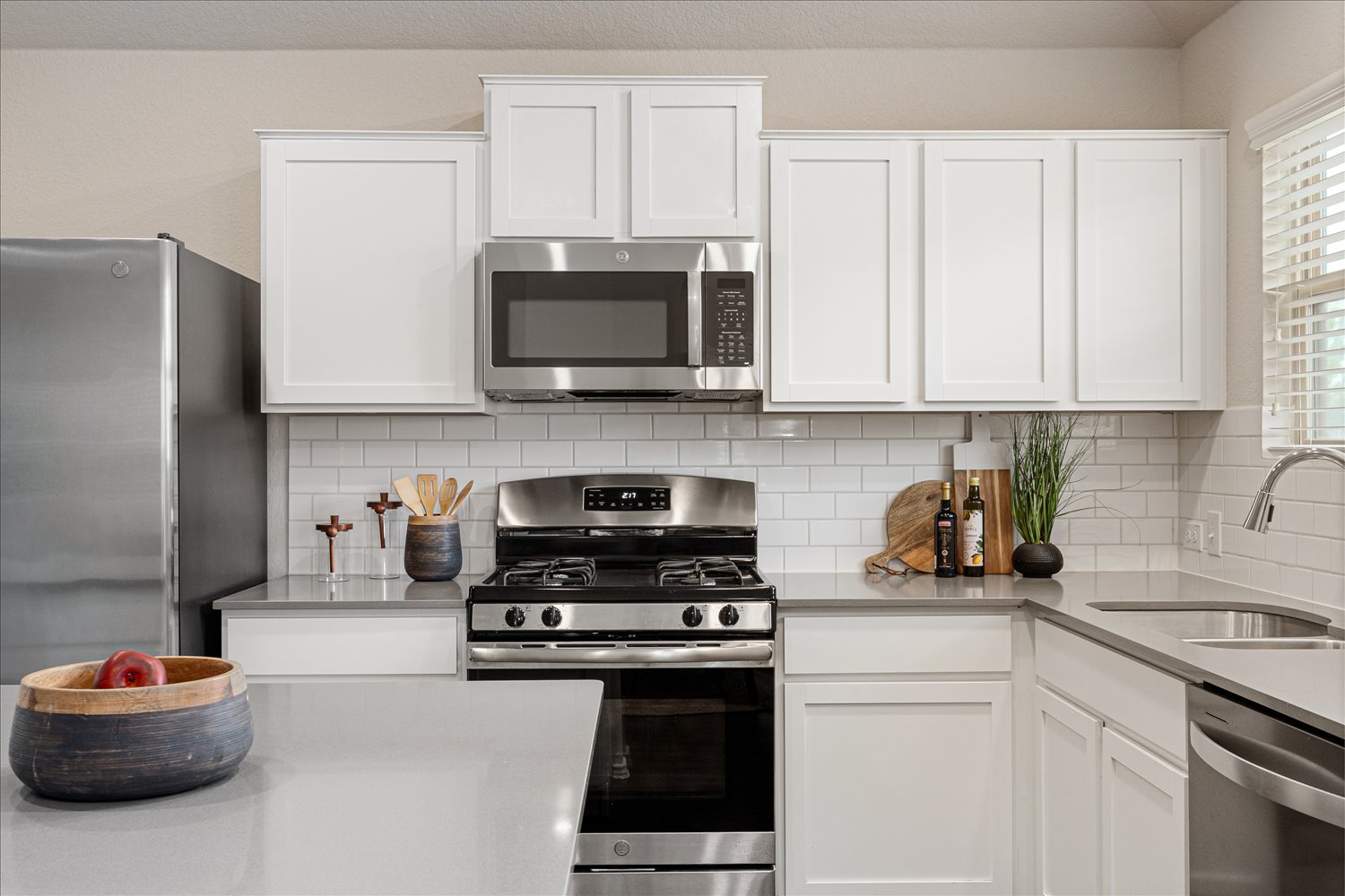 5812 Bell Tower Lane Austin, TX 78747 - Photo 9 of 24 Kitchen featuring stainless steel appliances, white cabinets, light stone countertops, and decorative backsplash