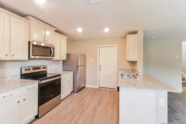 a kitchen with stainless steel appliances a stove top oven a sink a refrigerator white cabinets and wooden floor