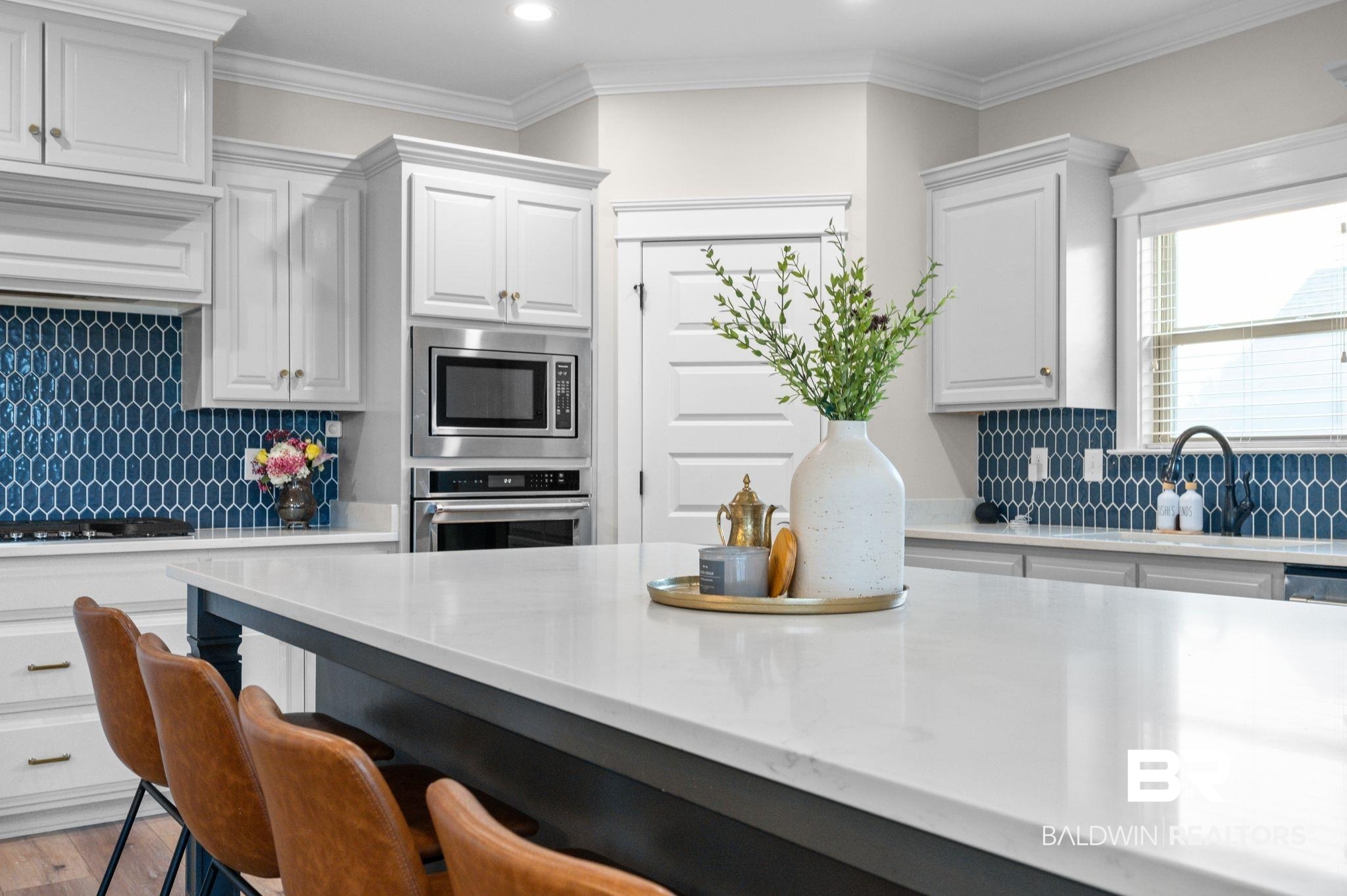 409 Fortune Drive Fairhope, AL 36532 - Photo 11 of 42 Spacious kitchen with a central island featuring a white countertop, white cabinetry with crown molding, a blue geometric tile backsplash, and stainless steel built-in appliances