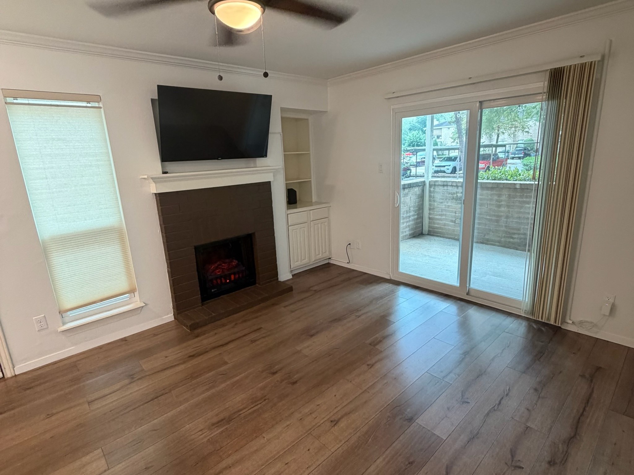 3500 Tangle Brush Drive, Unit 65 Spring, TX 77381 - Photo 9 of 20 Comfortable living area features a cozy fireplace with built-in shelving and cabinetry, crown molding, wood-look flooring, and sliding glass doors that fill the space with natural light and open to the private patio.