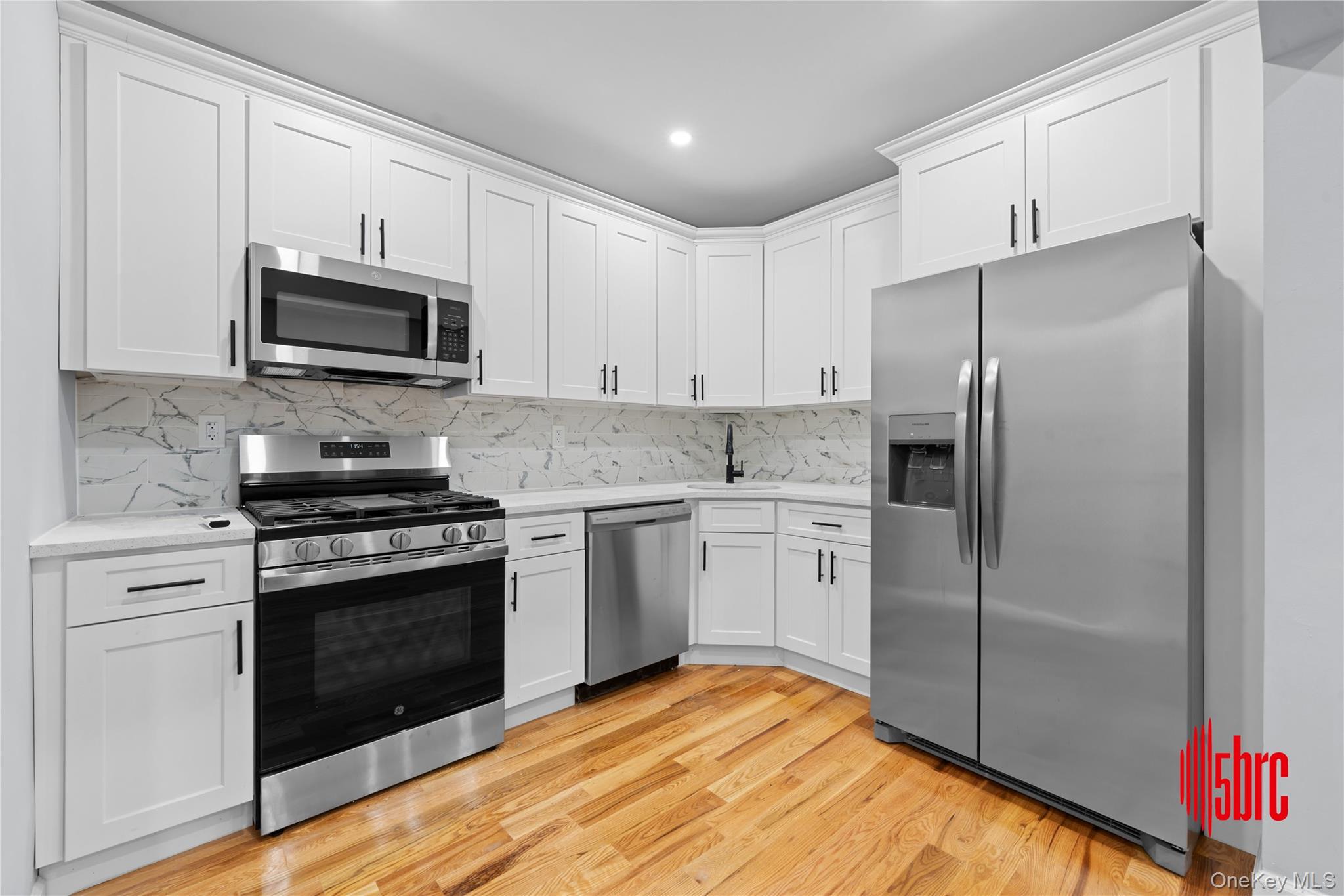 217-39 114th Road Queens, NY 11411 - Photo 4 of 23 Kitchen featuring stainless steel appliances, white cabinets, light wood finished floors, tasteful backsplash, and recessed lighting