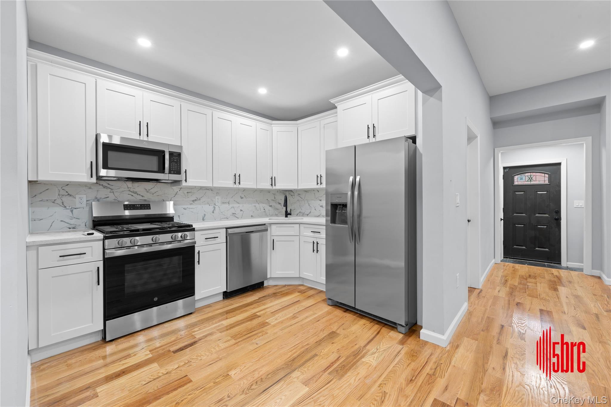 217-39 114th Road Queens, NY 11411 - Photo 5 of 23 Kitchen featuring appliances with stainless steel finishes, white cabinetry, light wood-type flooring, backsplash, and recessed lighting