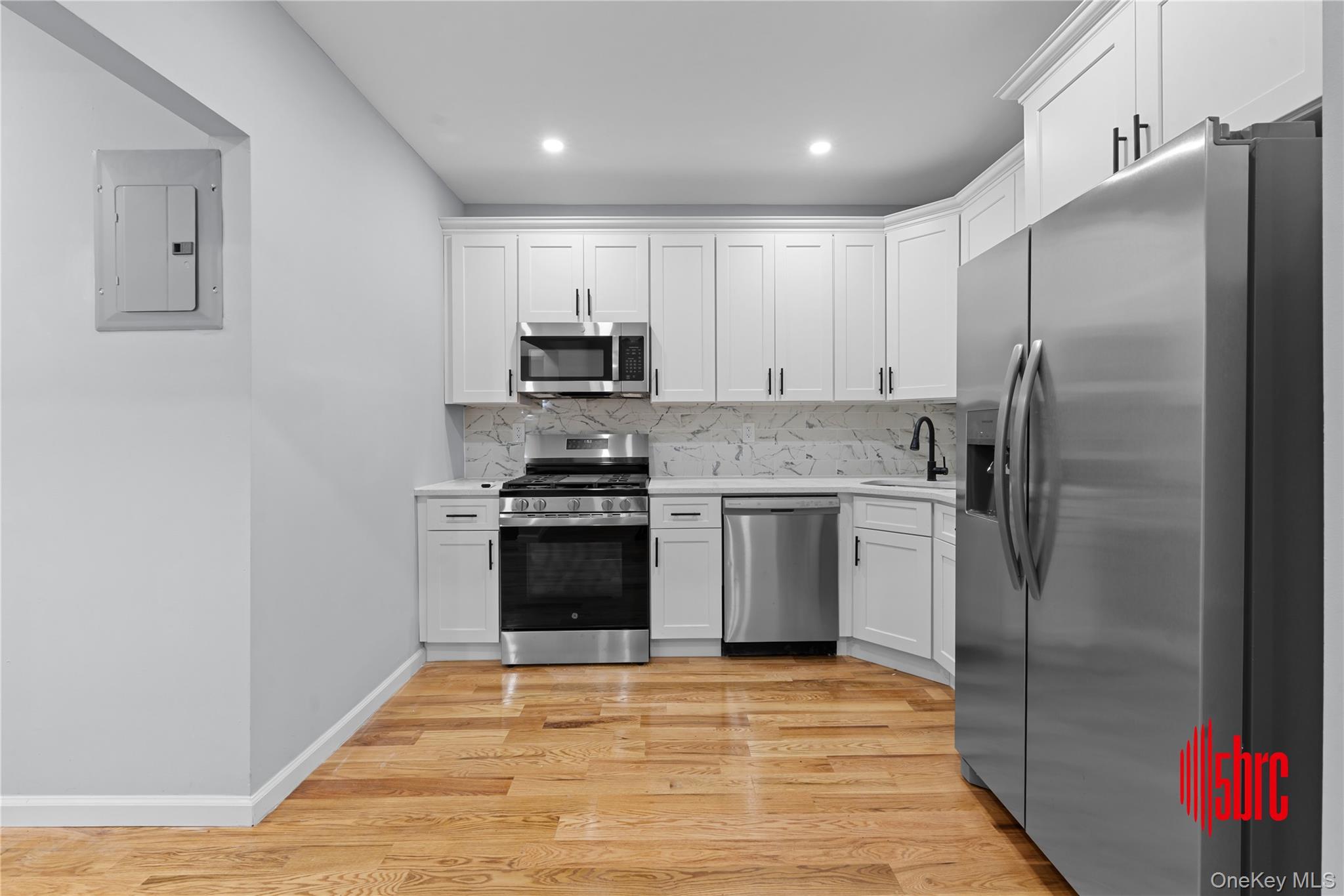 217-39 114th Road Queens, NY 11411 - Photo 6 of 23 Kitchen featuring stainless steel appliances, white cabinetry, electric panel, tasteful backsplash, and light wood-style flooring
