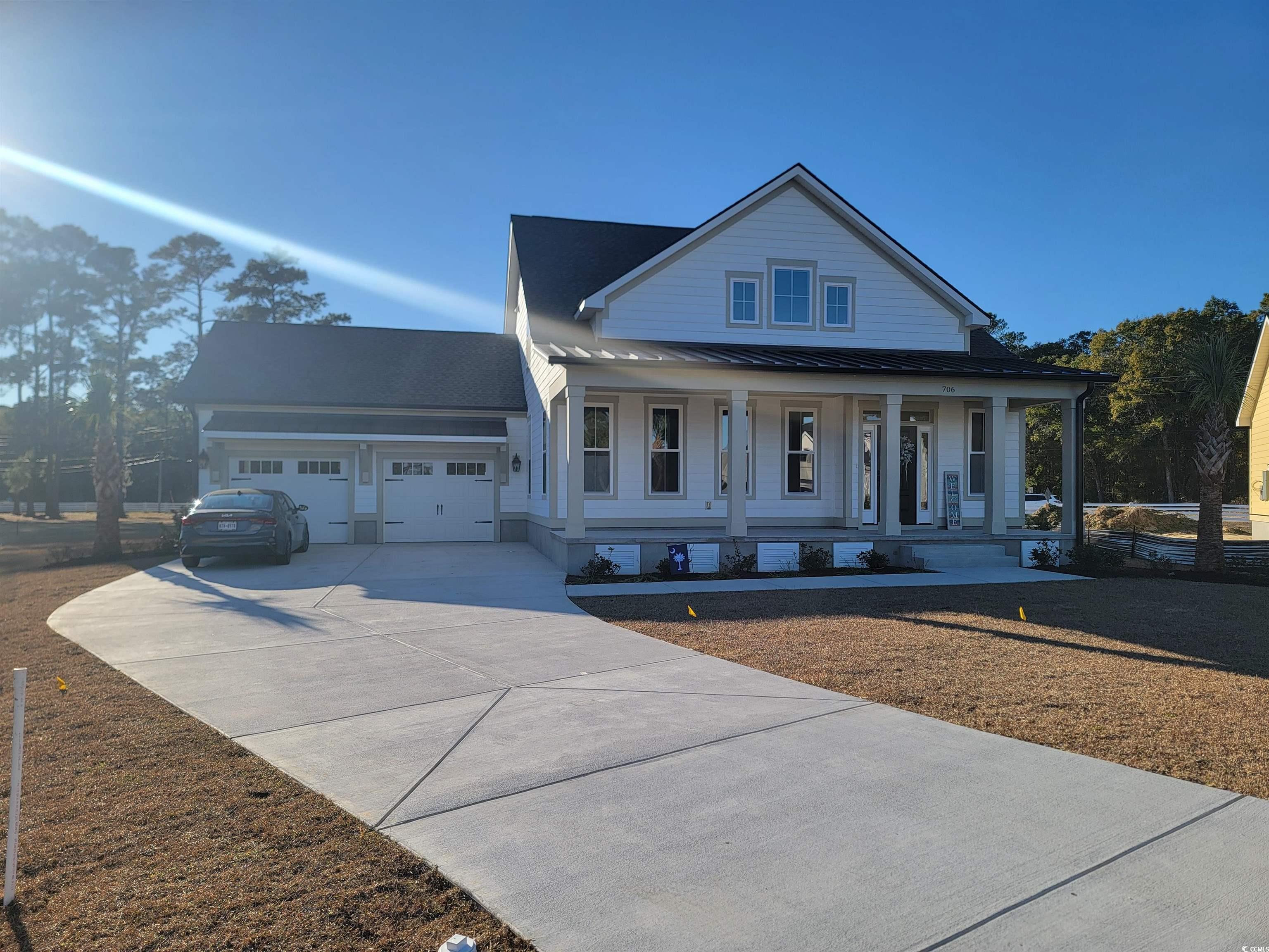 View of front of home with a standing seam roof, a metal roof, covered porch, concrete driveway, and an attached garage