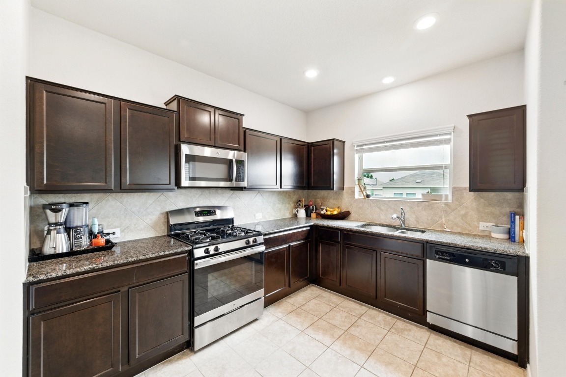 3905 Alpine Autumn Drive Austin, TX 78744 - Photo 4 of 24 Kitchen with light tile patterned flooring, dark brown cabinetry, appliances with stainless steel finishes, a sink, and decorative backsplash