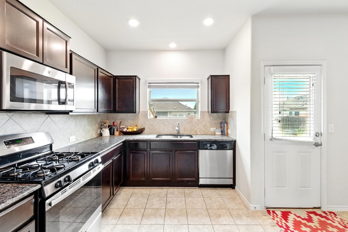 3905 Alpine Autumn Drive Austin, TX 78744 - Photo 8 of 24 Kitchen featuring dark brown cabinetry, appliances with stainless steel finishes, a sink, recessed lighting, and tasteful backsplash