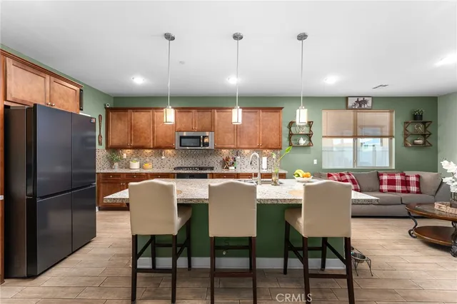 a kitchen with stainless steel appliances kitchen island granite countertop a dining table chairs refrigerator and sink