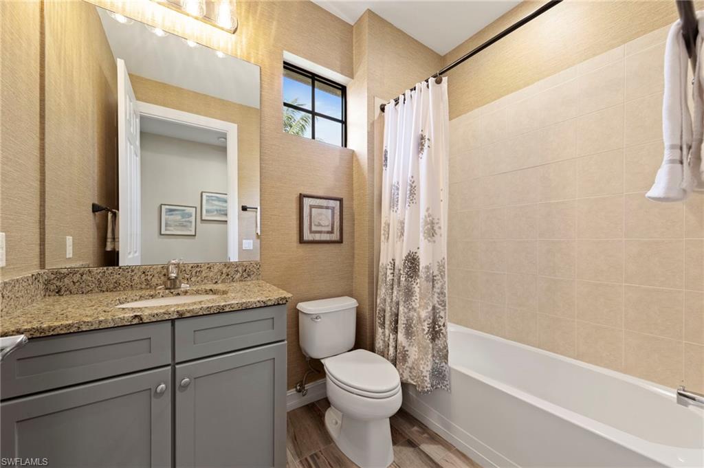 9076 Rialto Street, Unit 6204 Naples, FL 34113 - Photo 23 of 50 Hall bathroom featuring a granite-topped vanity with undermount sink, gray cabinetry, wood-finish tile flooring, and a window above the toilet. NEW TILE FLOOR (2018), NEW WALLPAPER (2018)