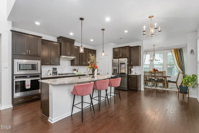 a kitchen with stainless steel appliances kitchen island granite countertop a stove top oven a refrigerator a sink and chairs with wooden floor