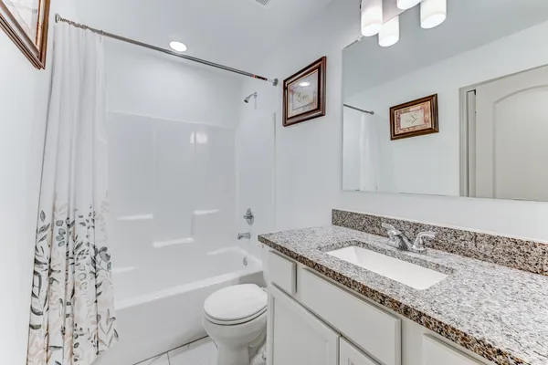 a bathroom with a granite countertop sink a toilet a shower curtain and a bath tub