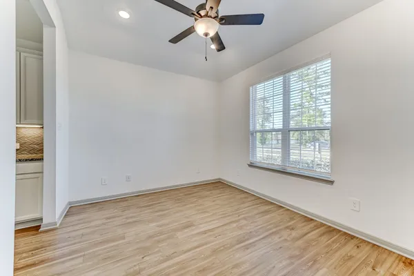 an empty room with wooden floor chandelier fan and windows