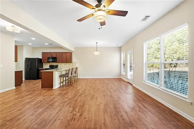 a open kitchen with stainless steel appliances kitchen island granite countertop a refrigerator a stove top oven a dining table and chairs with wooden floor
