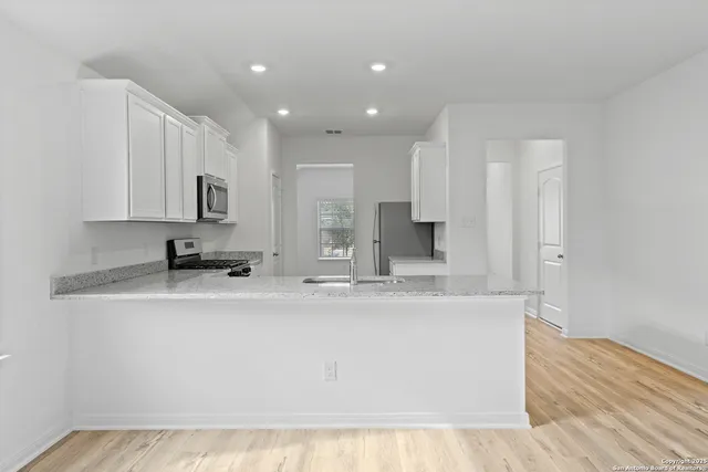 a large kitchen with stainless steel appliances granite countertop a stove a sink a refrigerator and white cabinets with wooden floor