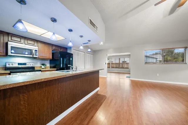 a open kitchen with stainless steel appliances granite countertop a refrigerator a sink dishwasher a stove and a dining table with wooden floor