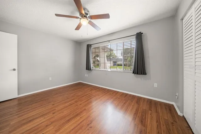 an empty room with wooden floor fan and windows