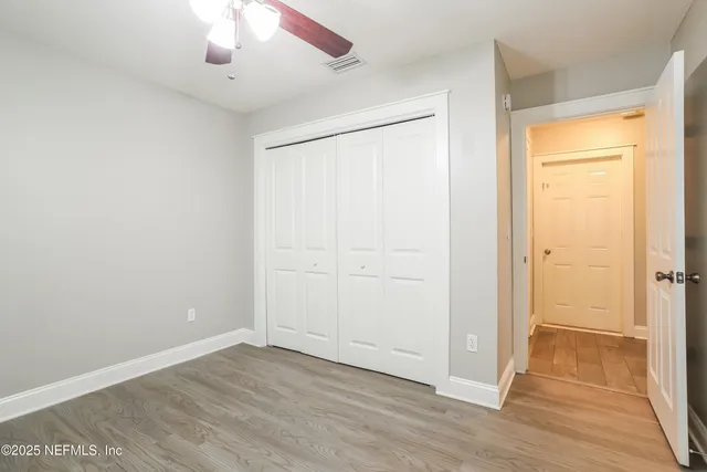 an empty room with a chandelier fan and kitchen view