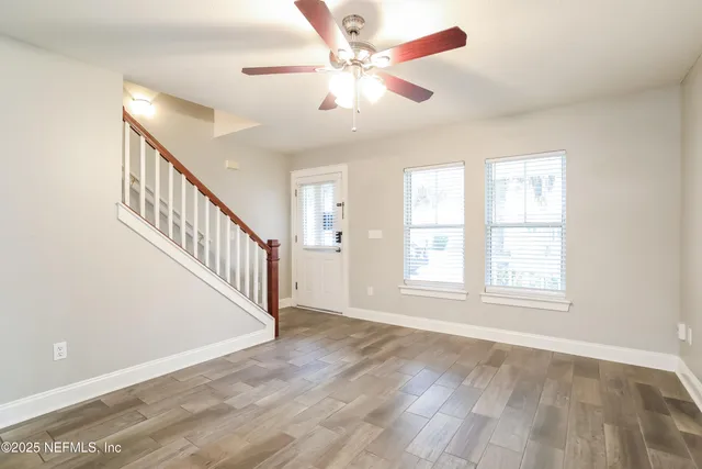 an empty room with wooden floor fan and windows