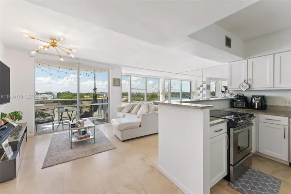 a living room with kitchen island furniture a chandelier a large window and a fireplace