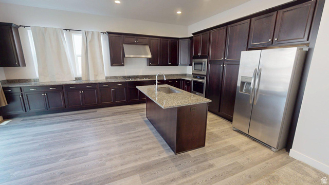 5502 North Valley View Road Lehi, UT 84048 - Photo 6 of 33 Spacious kitchen featuring extensive dark wood cabinetry, light wood-finish flooring, a central island with a sink, stainless steel appliances, and ample countertop space