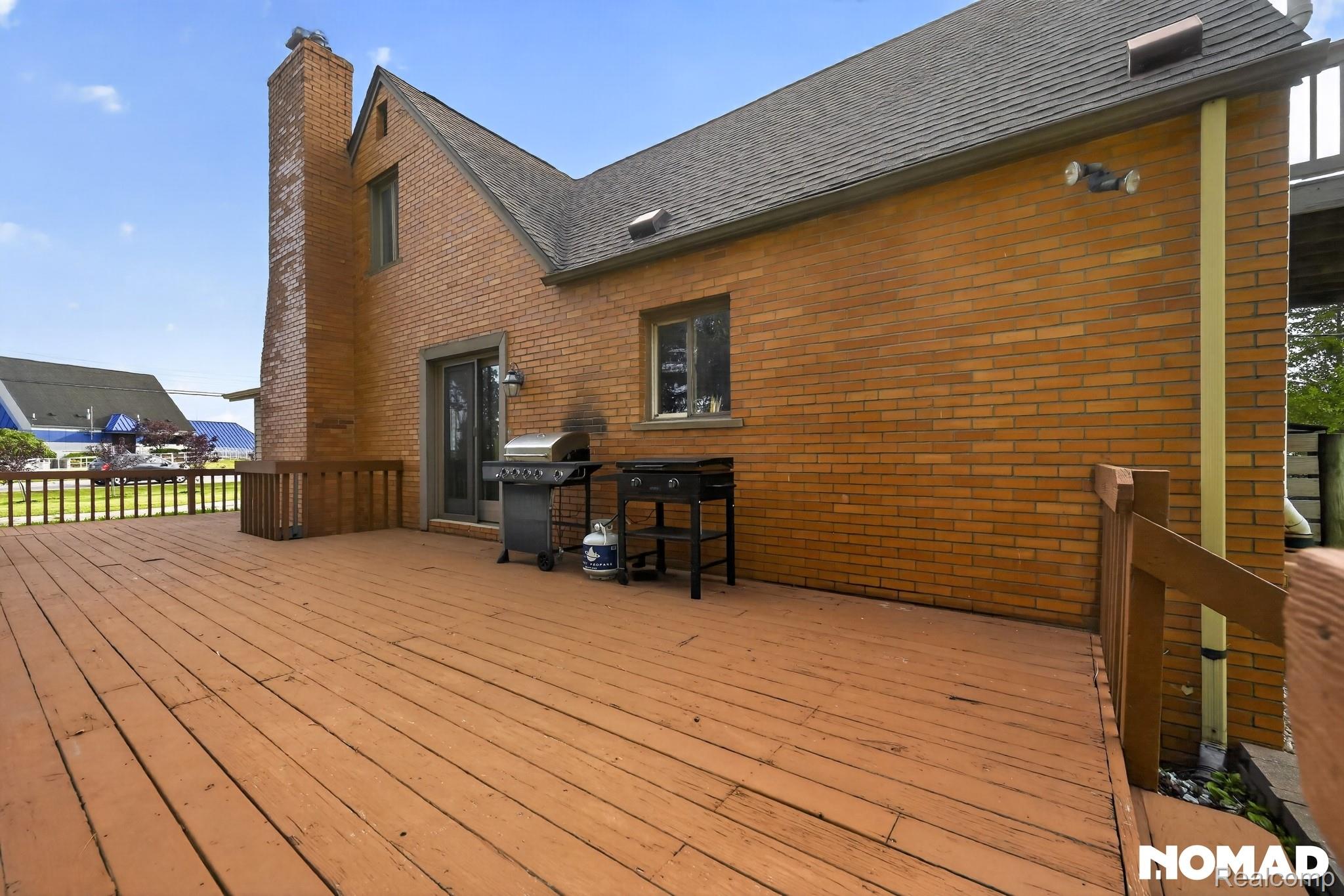 8315 Hilton Road Brighton, MI 48114 - Photo 3 of 26 Expansive wood-finish deck with integrated railing, full brick exterior, and a prominent brick chimney