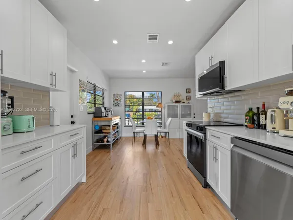 a kitchen with stainless steel appliances granite countertop a refrigerator oven a sink dishwasher and white cabinets with wooden floor