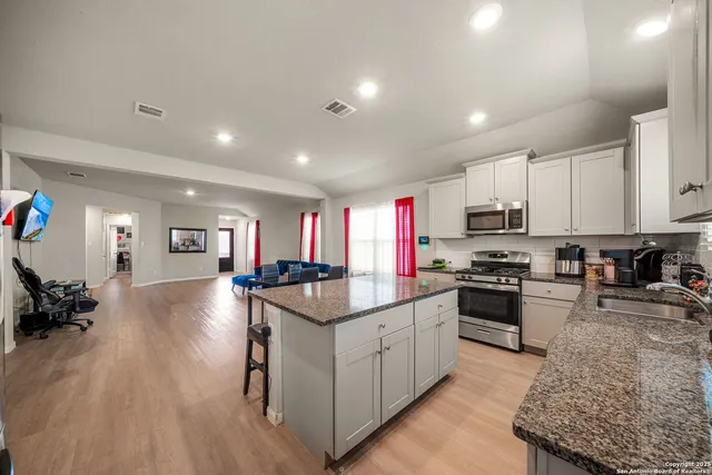 a kitchen with stainless steel appliances granite countertop a stove top oven a sink dishwasher and a refrigerator with wooden floor