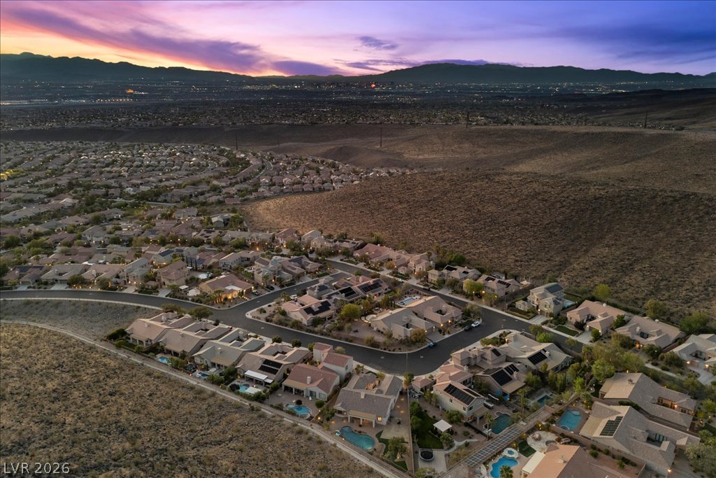 2125 De Rouge Avenue Henderson, NV 89044 - Photo 90 of 96 An aerial perspective reveals a vibrant neighborhood nestled against a sweeping desert landscape at dusk.