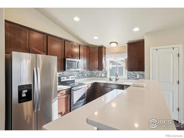 a view of an empty room with wooden floor and a kitchen