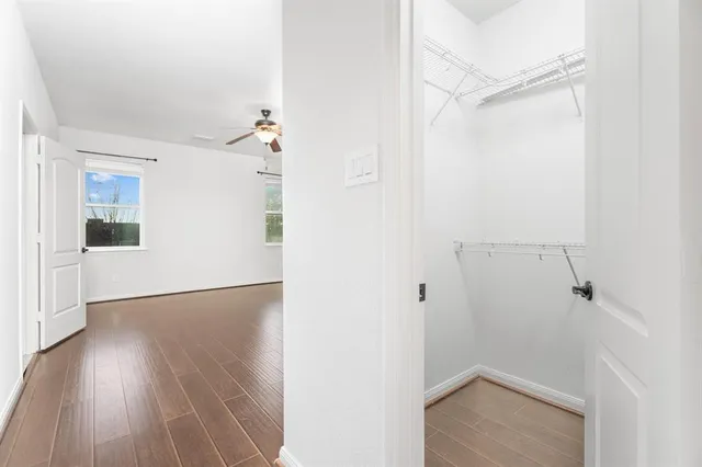 an empty room with wooden floor ceiling fan and windows