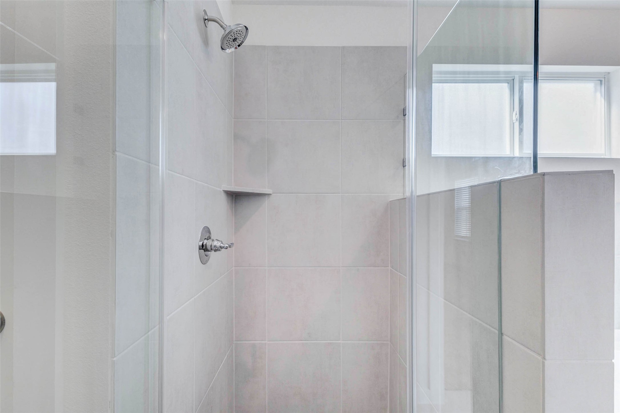 6467 Escondido Drive Rosharon, TX 77583 - Photo 22 of 32 Close-up of the primary walk-in shower featuring neutral tile walls, glass enclosure, chrome fixtures, built-in corner shelf, and a frosted privacy window nearby. The shower’s clean design and bright finish create a fresh, low-maintenance bath feature with modern appeal.