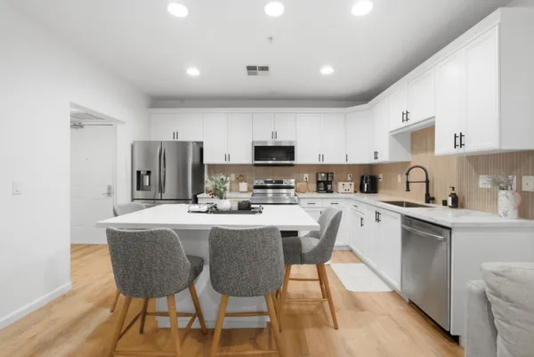 a kitchen with stainless steel appliances granite countertop a dining table chairs refrigerator sink and cabinets