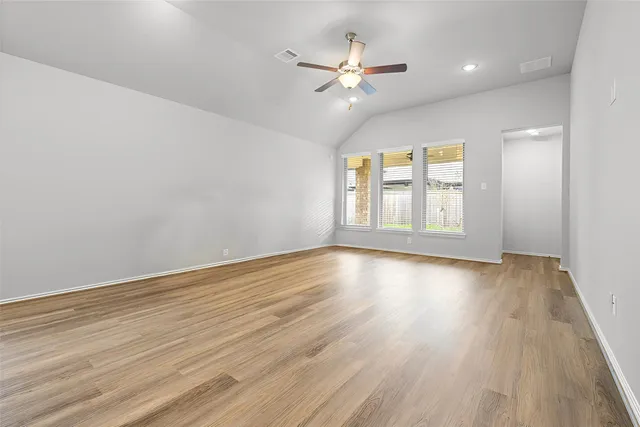a view of an empty room and kitchen view with wooden floor