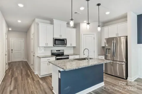 a kitchen with granite countertop a refrigerator a sink dishwasher a stove and white cabinets with wooden floor