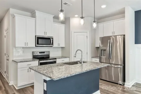 a kitchen with stainless steel appliances granite countertop a refrigerator a stove a sink and a microwave with wooden floor