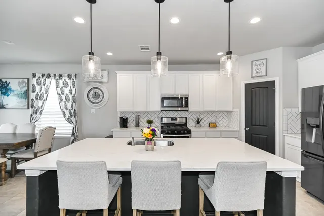 a kitchen with stainless steel appliances a dining table chairs refrigerator and microwave