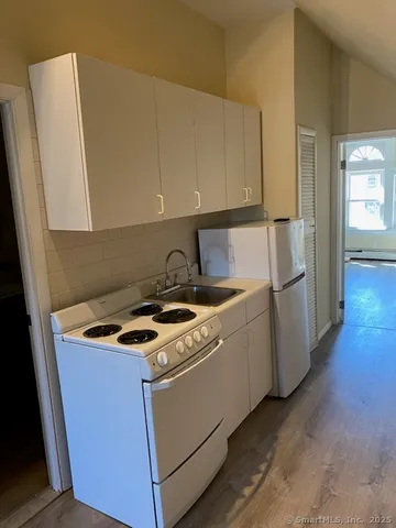 a kitchen with granite countertop a refrigerator a sink a stove and white cabinets