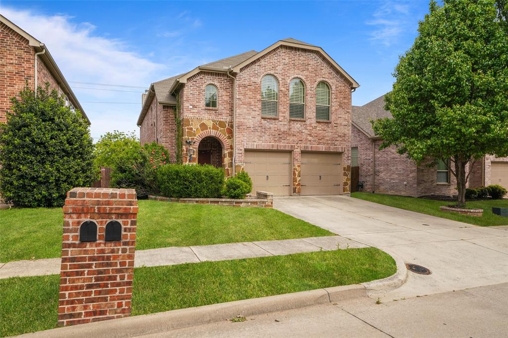 View of front of house with brick siding, a garage, driveway, and a front lawn