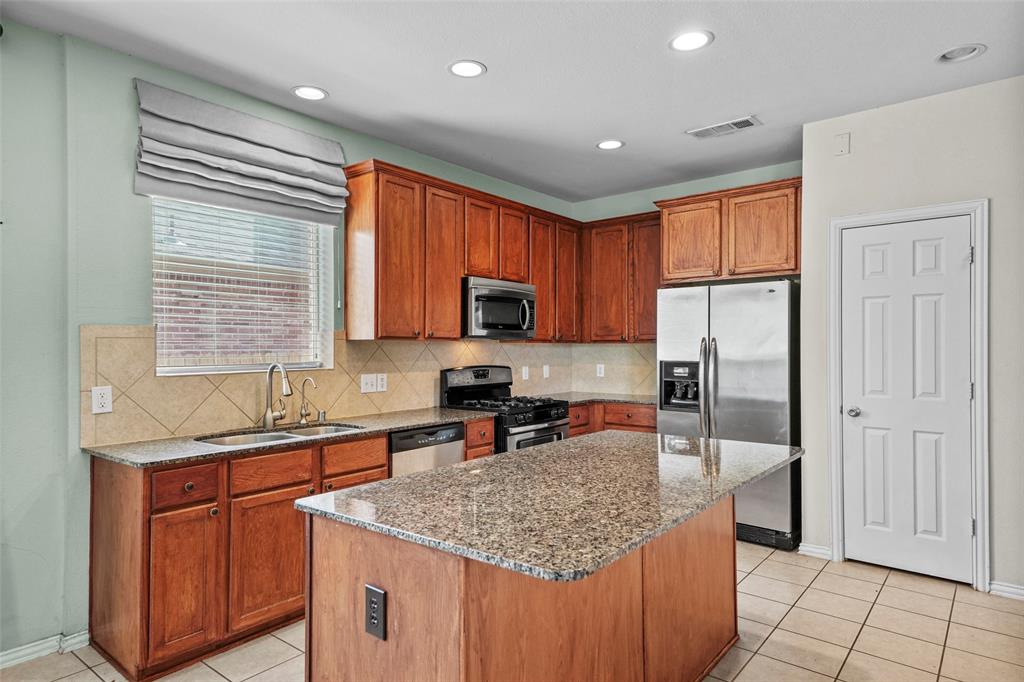 2405 Reston Drive McKinney, TX 75072 - Photo 11 of 38 Kitchen featuring dark stone counters, stainless steel appliances, light tile patterned floors, a center island, and decorative backsplash