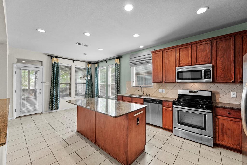 2405 Reston Drive McKinney, TX 75072 - Photo 10 of 38 Kitchen with dark stone counters, stainless steel appliances, light tile patterned floors, decorative backsplash, and a kitchen island