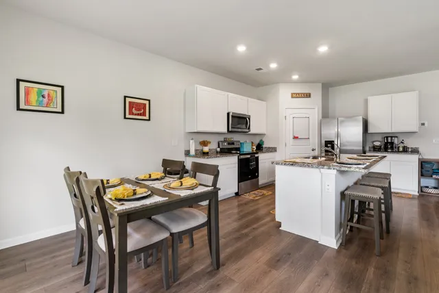 a kitchen with stainless steel appliances granite countertop a sink a stove a refrigerator and a dining table with wooden floor