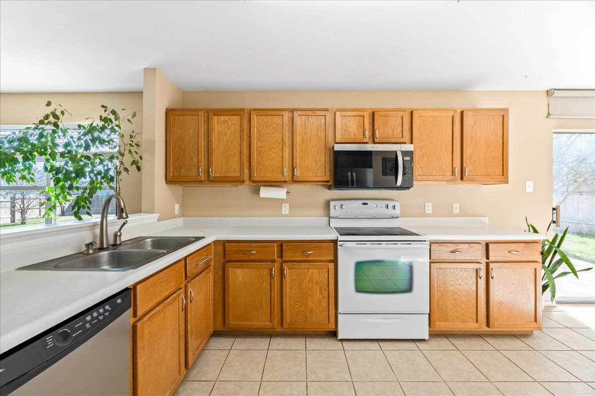 116 Devon's Cove Buda, TX 78610 - Photo 22 of 38 Kitchen with stainless steel appliances, light countertops, light tile patterned floors, and wood finish cabinets
