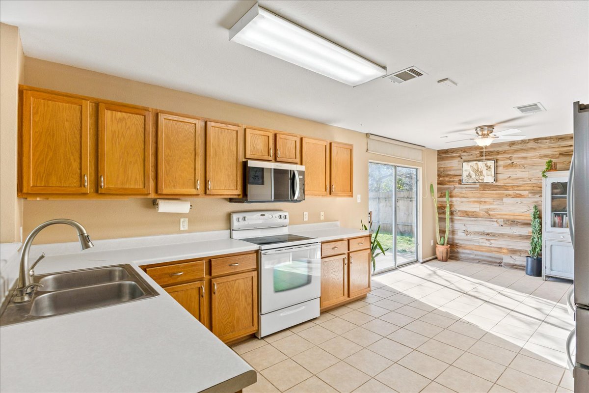 116 Devon's Cove Buda, TX 78610 - Photo 24 of 38 Kitchen with stainless steel appliances, wooden walls, light countertops, ceiling fan, and light tile patterned floors