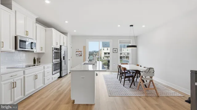 a open kitchen with stainless steel appliances kitchen island granite countertop a refrigerator a stove a sink a dining table and chairs with wooden floor
