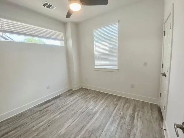 an empty room with wooden floor chandelier fan and windows