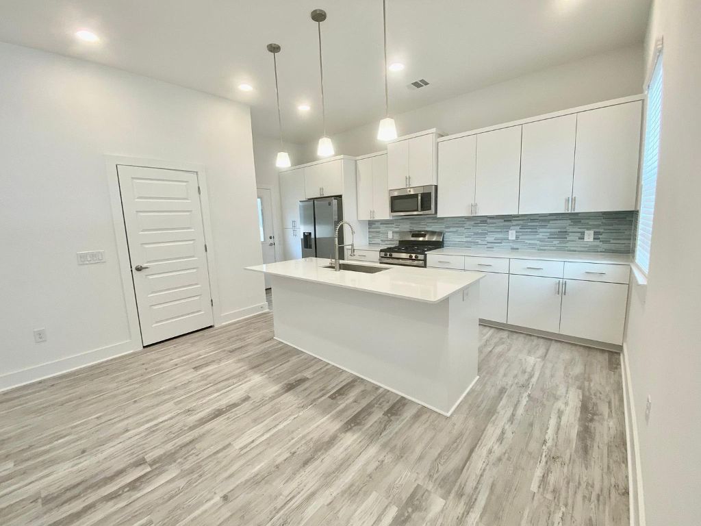 6809 Montana Street, Unit 2 Austin, TX 78741 - Photo 3 of 29 a large white kitchen with kitchen island a sink dishwasher a stove and a refrigerator with wooden floor